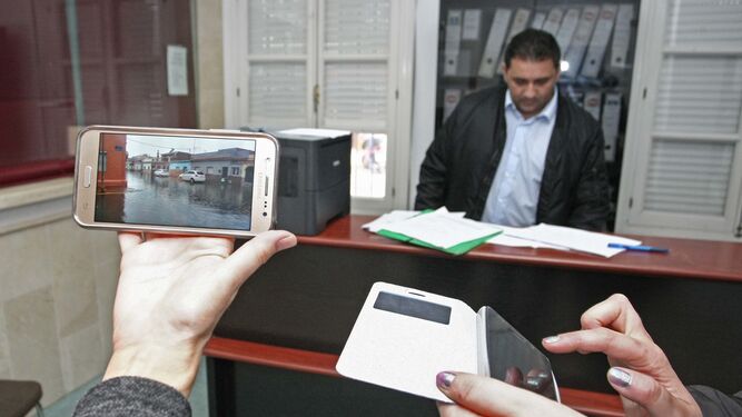 Dos personas muestran en sus móviles los daños sufridos en sus propiedades en la oficina habilitada para ello en La Línea.