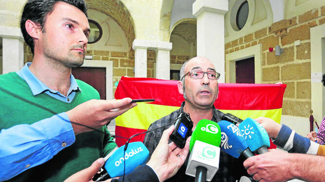 Martín Aubarrea habla a los medios mientras que una mujer despliega detrás una bandera de España en la Casa de Iberoamérica.