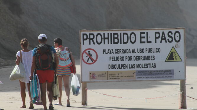 Tres bañistas acceden a una de las zonas prohibidas haciendo caso omiso al cartel de advertencia que tienen al lado.