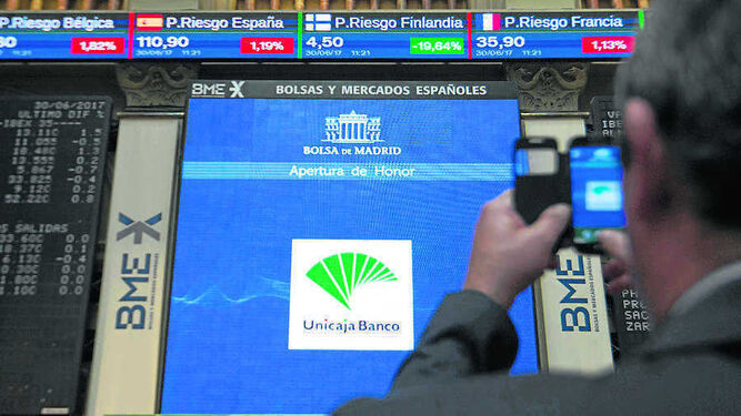 Un hombre fotografía la pantalla con los valores y la entrada de Unicaja a Bolsa.