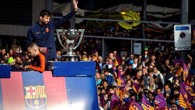 El capitán Gerard Piqué saluda a la afición desde el autobús descapotable con el trofeo de La Liga presidiendo la escena.