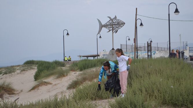 Dos personas recogen basura junto a la playa de Los Lances, en Tarifa.