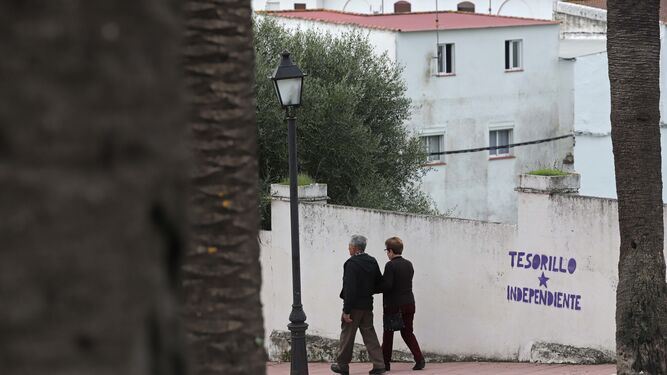Dos lugareños caminan por una calle de San Martín del Tesorillo junto a una vieja pintada que reclama la independencia de Jimena de la Frontera.