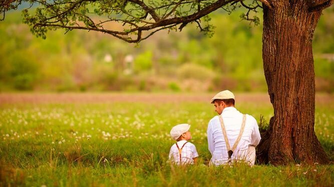 Un padre y un hijo conversando en un prado.