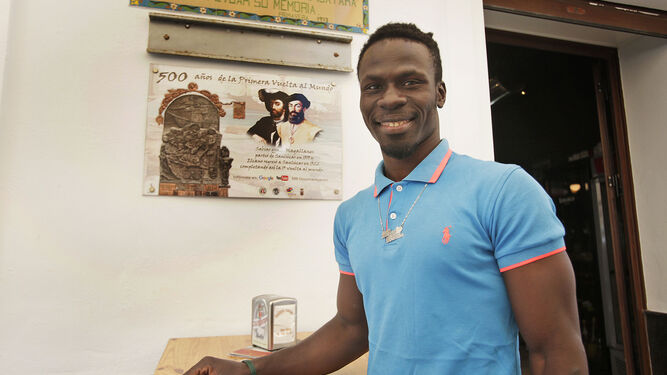 Un vendedor ambulante senegalés posa ante una de las placas de la conmemoración de la primera vuelta al mundo