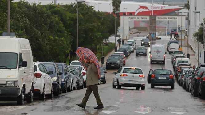 Un hombre cruza una calle en Tarifa cubierto por un paraguas.