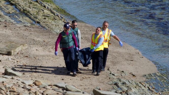 Cuatro personas recogen el cadáver de Óscar Maquera en la costa, este martes.