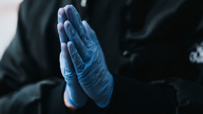 Una persona reza con unos guantes médicos de protección.