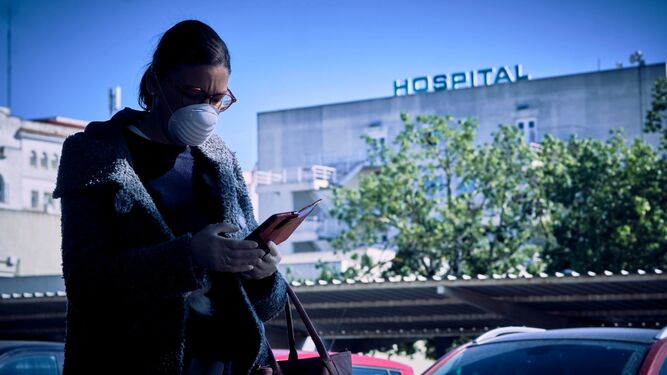 Una mujer, con guantes y mascarillas, usa el teléfono a las puertas de un hospital