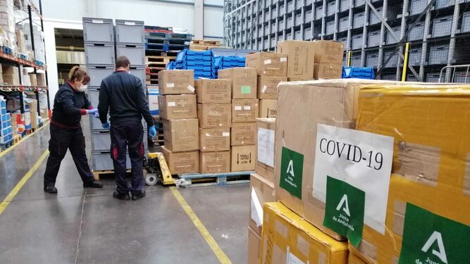 Dos operarios descargan material sanitario en el almacén logístico de la Junta en el Puerto de Sevilla