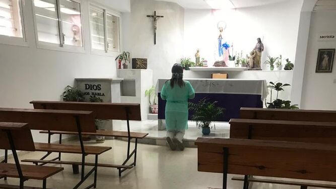 Una enfermera con bata y mascarilla reza arrodillada en la capilla del Hospital de Puerto Real.
