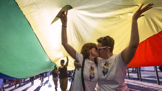 Dos mujeres se besan bajo la bandera arcoiris en una manifestación del Orgullo.