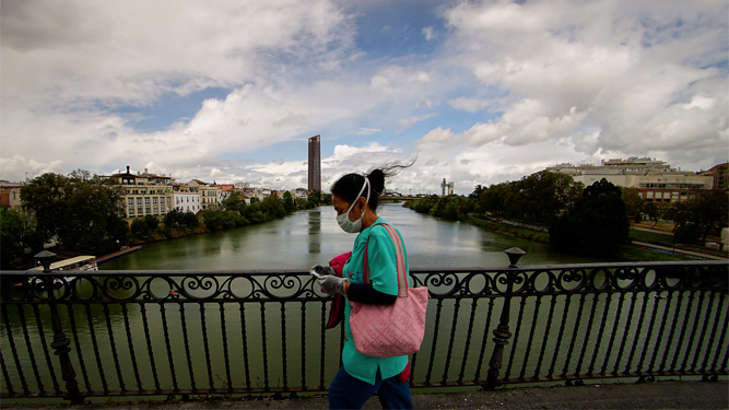 Una mujer protegida con mascarilla y guantes atraviesa el Puente de Triana.