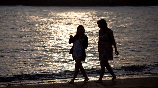 Dos mujeres pasean en pleno atardecer en la playa de La Malagueta, en Málaga.