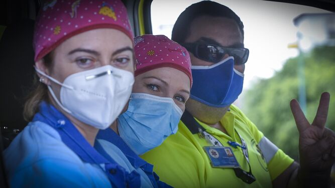 Tres sanitarios saludan enfundados en sus mascarillas en el interior de una ambulancia.