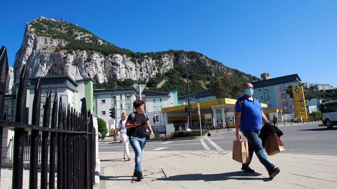 Tres personas caminan en Gibraltar, con el peñón al fondo.