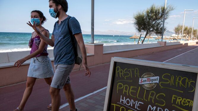 Dos jóvenes pasan ante el cartel de un bar en Baleares.