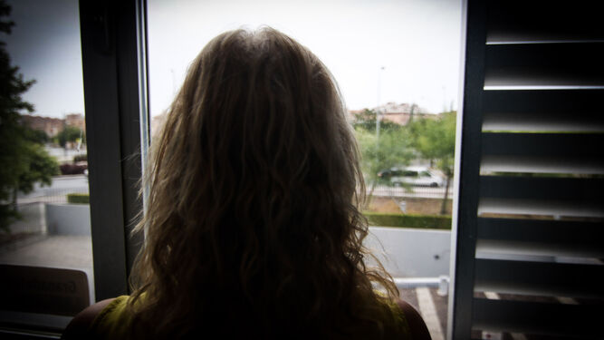 Una mujer, de espaldas, asomada a una ventana.