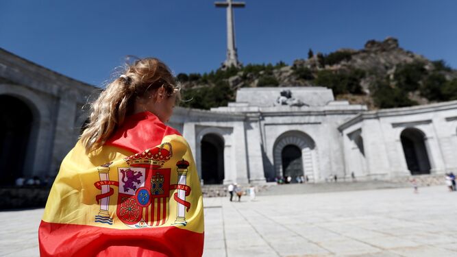 Una mujer envuelta en una bandera nacional ante la entrada de la basílica del Valle de los Caídos.