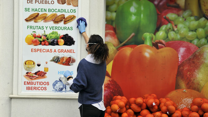 Una mujer desinfectando un cartel en un supermercado en Arcos