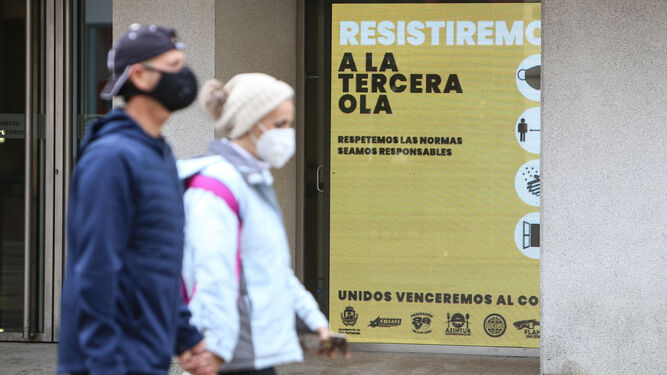Una pareja con sus mascarillas pasa junto a un cartel del Ayuntamiento isleño alusivo a la pandemia.