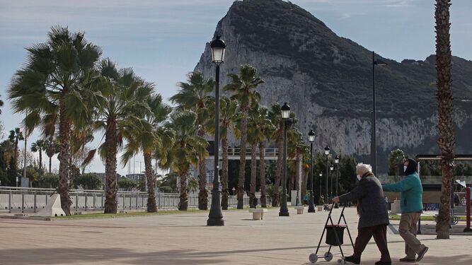 Dos personas pasean en La Línea, con el Peñón de Gibraltar al fondo.