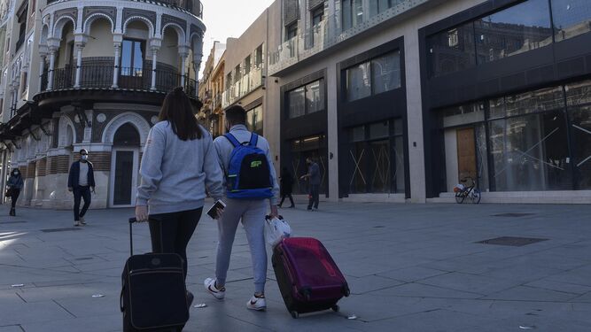Varios turistas pasan por la Avenida de la Constitución con sus maletas.