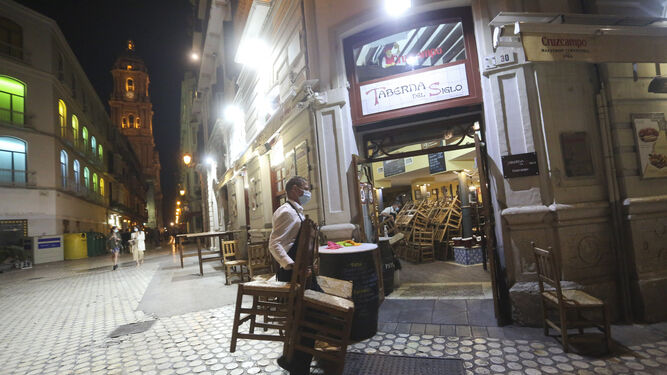 Un camarero recoge las sillas en un bar de Málaga.