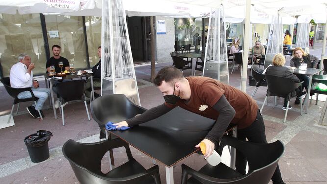 Un camarero desinfecta una mesa en una terraza de Algeciras.