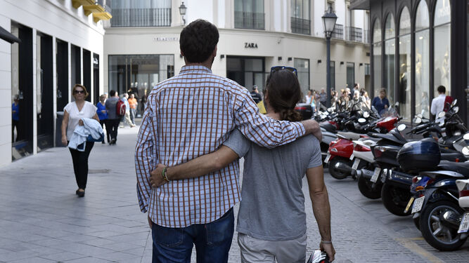 Una pareja de hombres camina abrazada por la calle.