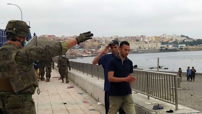 Un miembro del Ejército de Tierra da instrucciones a un grupo de inmigrantes en uno de los espigones fronterizos de Ceuta.