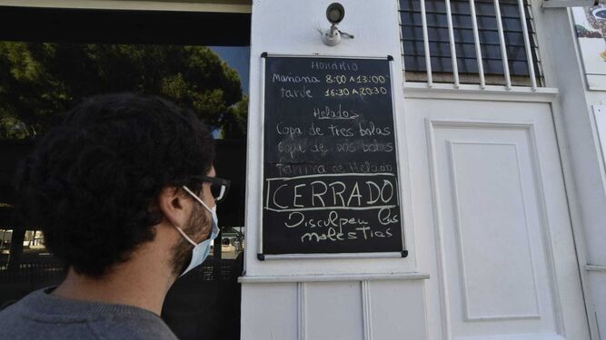 Una persona observa el cartel que anuncia el cierre de la cafetería Plum Cake, en San Roque.