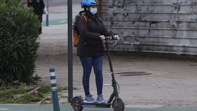 Una mujer protegida con casco circula con un patinete por un carril bici.