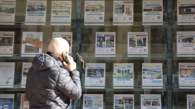 Un transeunte pasa por una inmobiliaria con carteles de viviendas en venta