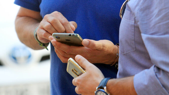 Dos hombres con su teléfono móvil en la mano.