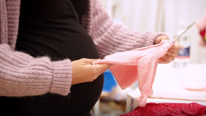 Una embarazada elige ropa para el bebé.