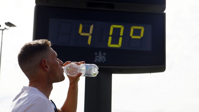 Un hombre bebe agua frente a un termómetro en Córdoba.