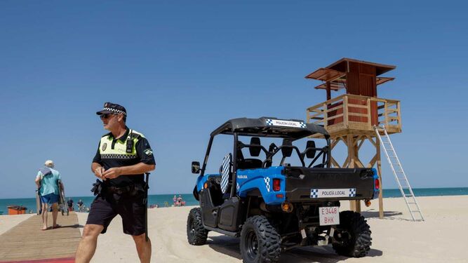 Un agente de la Policía Local esta mañana en la playa Victoria junto a un vehículo de patrulla.