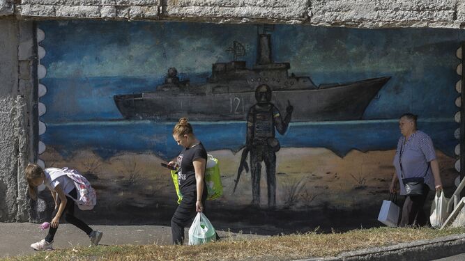 Varias personas pasan ante un mural en Kiev que muestra a un soldado ucraniano gesticulando hacia un barco de guerra ruso.