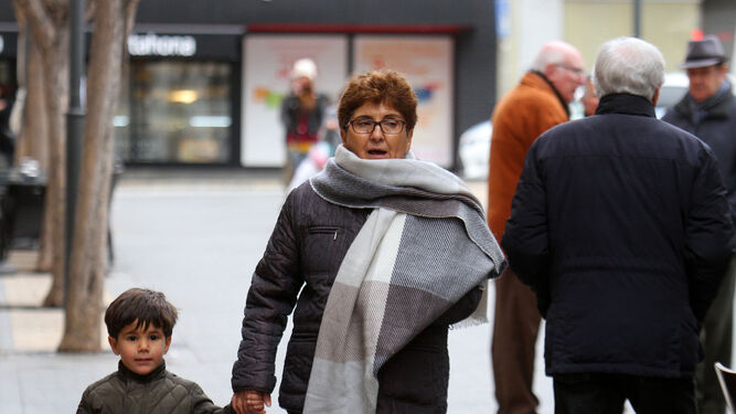 Una mujer y su nieto caminan por el centro de Huelva abrigados con chaquetones y bufanda.